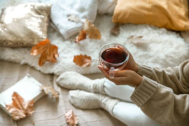 Przytulna jesień w domu, kobieta z herbatą i książkowym odpoczynkiem. Przytulny styl życia. Części ciała w składzie. - Zdjęcie, obraz