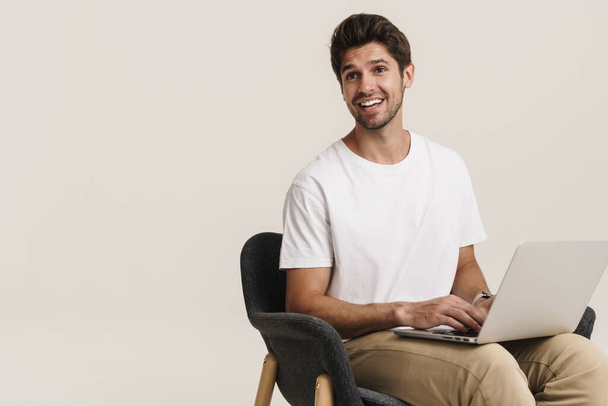 Portrait of unshaven excited man working with laptop while sitting on armchair isolated over white background - Foto, imagen
