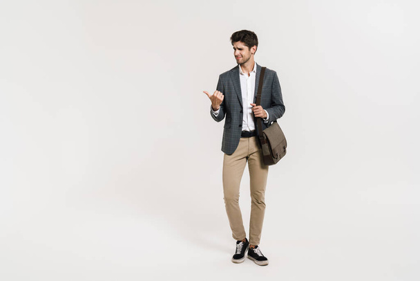 Photo of confused caucasian businessman pointing finger aside while posing with bag isolated over white wall - Foto, afbeelding