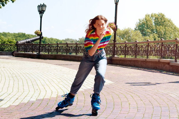 Teenage dívka v krásné světlé tričko a džíny je brusle v parku - Fotografie, Obrázek