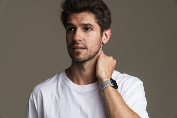 Portrait of confident young man in basic t-shirt posing and looking aside isolated over grey background - Photo, Image