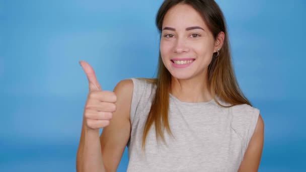 Schöne positive Frau im grauen T-Shirt zeigt Daumen hoch, wie und lächelt - Filmmaterial, Video