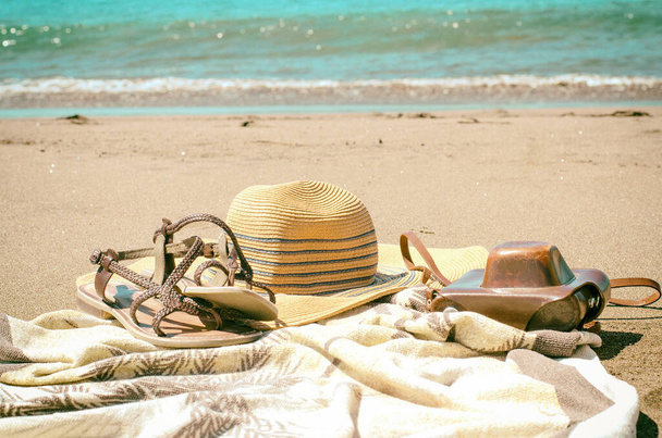 Summer accessories on sandy beach: straw hat, sandals and camera. Concept for travel or vacation. Vintage style. - Photo, Image