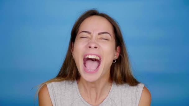 Schöne Frau in grauem T-Shirt schreit auf blauem Hintergrund mit Kopierraum - Filmmaterial, Video