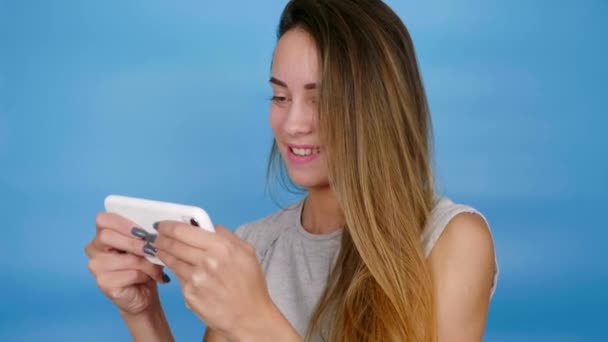 Emotional positive woman gamer plays video game on smartphone, smiles, has fun - Video, Çekim