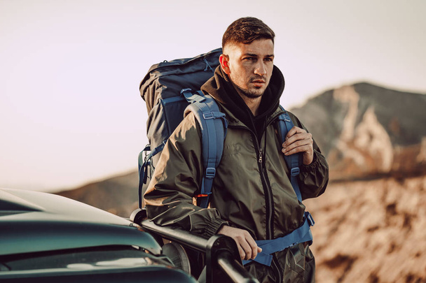 Portrait of a young traveler man in hiking equipment standing near his off-road car - Foto, afbeelding