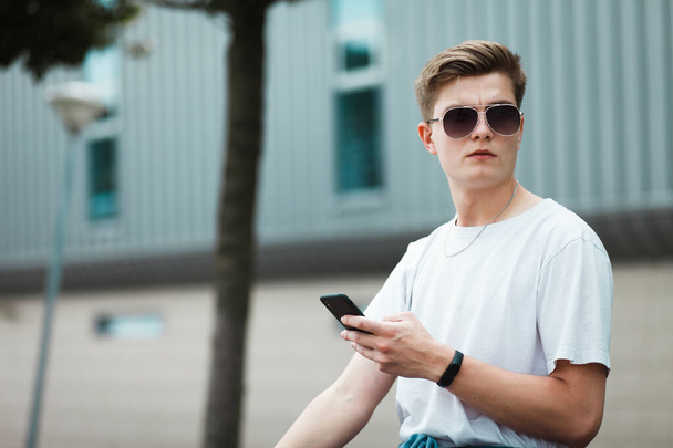 İnternette akıllı telefonuyla bankta oturan yakışıklı genç adam. - Fotoğraf, Görsel