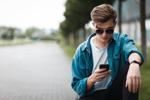 Knappe jongeman zittend op een bank met een smartphone op het internet - Foto, afbeelding