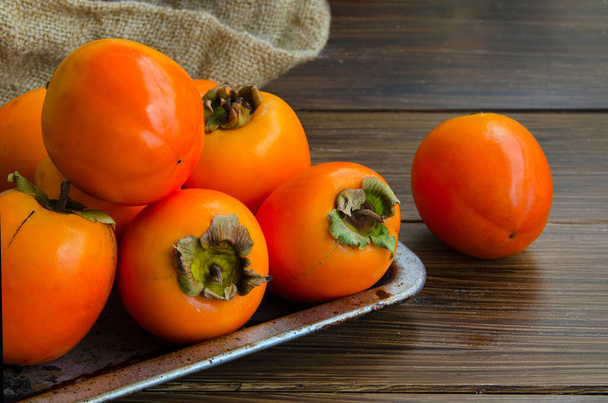 Fresh organic persimmon in vintage metal plate on rustic wood background. Concept for healthy food, vegan or raw diet. - Foto, Imagem