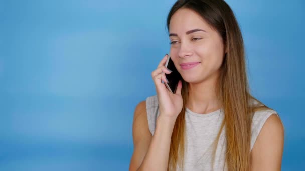 Gelukkig vrouw in grijs T-shirt houdt smartphone in de buurt van oor, luistert vriendje, lacht - Video
