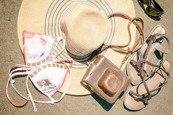 Accessori estivi sulla spiaggia sabbiosa: cappello di paglia, sandali e macchina fotografica. Concetto per viaggi o vacanze. Stile vintage. - Foto, immagini