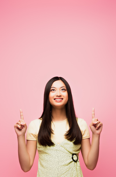 vidám ázsiai lány ujjal mutogat, és felnéz elszigetelt rózsaszín  - Fotó, kép