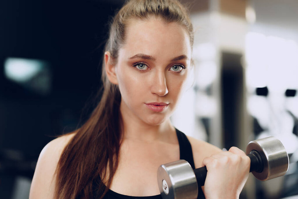 Young brunette sporty woman exercising with dumbbell in a gym - 写真・画像