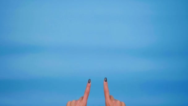 Manos de mujer apuntando al espacio de copia, mostrando pulgares hacia arriba, como sobre fondo azul - Imágenes, Vídeo