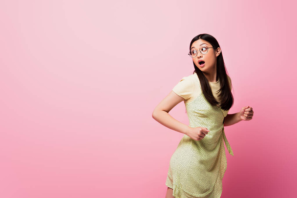 geschokt aziatische vrouw in bril lopen en weg te kijken op roze  - Foto, afbeelding