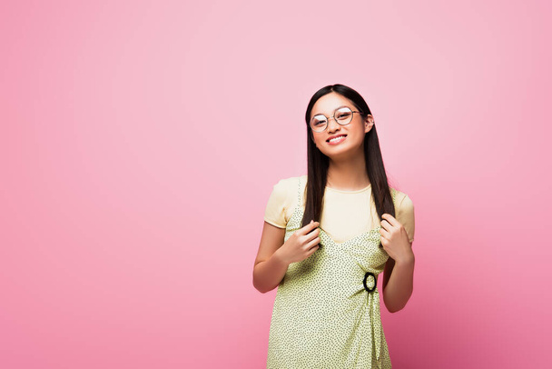 cheerful and young asian woman in glasses smiling on pink - Foto, imagen