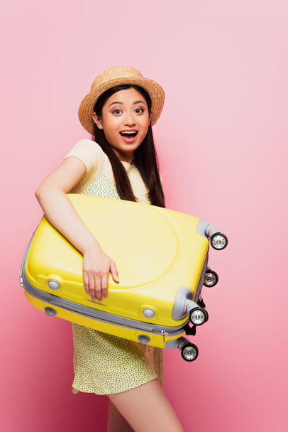 excited asian girl in straw hat holding luggage on pink  - Fotoğraf, Görsel