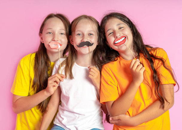 Щасливі діти тримають підроблені вуса і губи на рожевому тлі. Салон краси. Салон дизайну волосся. Салонний фоторобот
.  - Фото, зображення