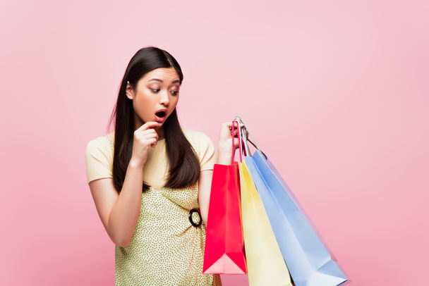 shocked asian girl looking at shopping bags isolated on pink  - Fotoğraf, Görsel