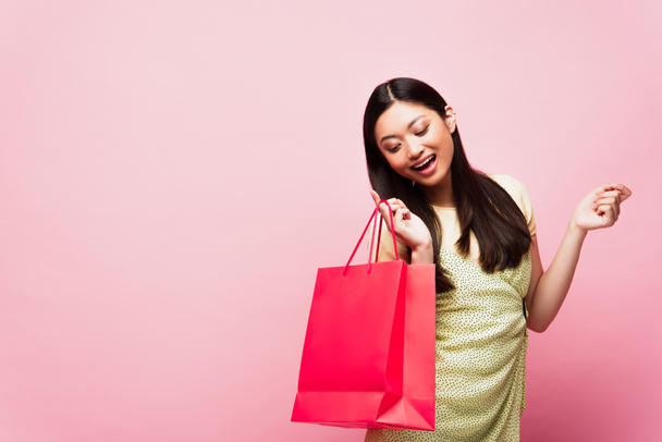 Gülümseyen genç Asyalı kadın pembe alışveriş çantasına bakıyor.  - Fotoğraf, Görsel