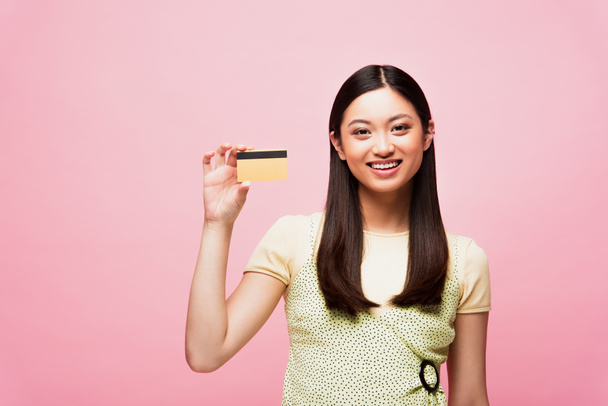 smiling young asian woman holding credit card isolated on pink  - Фото, зображення