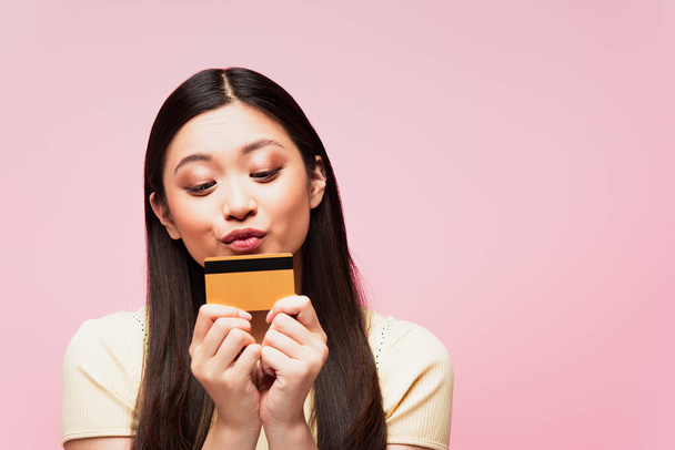 attractive and young asian woman kissing credit card isolated on pink  - Фото, изображение