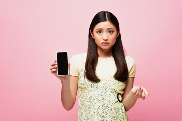 upset asian woman holding smartphone with blank screen isolated on pink  - Fotografie, Obrázek