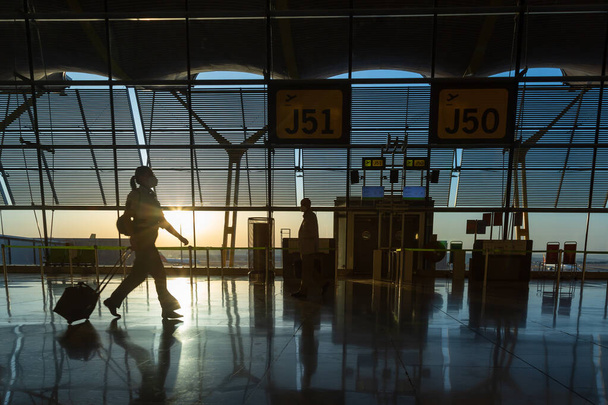 Tunnistamattoman naisen siluetti matkalaukkunsa kanssa lentokentällä lähtöterminaalissa auringon noustessa. - Valokuva, kuva
