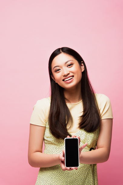 šťastná asijská žena držící smartphone s prázdnou obrazovkou izolované na růžové  - Fotografie, Obrázek