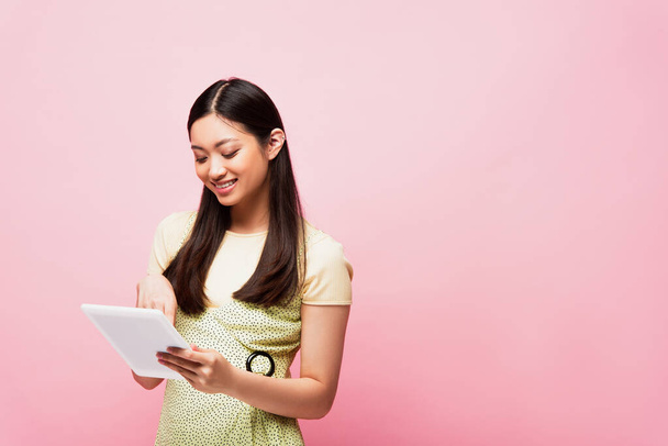 iloinen aasialainen tyttö käyttäen digitaalinen tabletti eristetty vaaleanpunainen  - Valokuva, kuva
