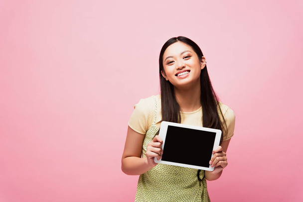 iloinen aasialainen tyttö tilalla digitaalinen tabletti tyhjä näyttö eristetty vaaleanpunainen  - Valokuva, kuva
