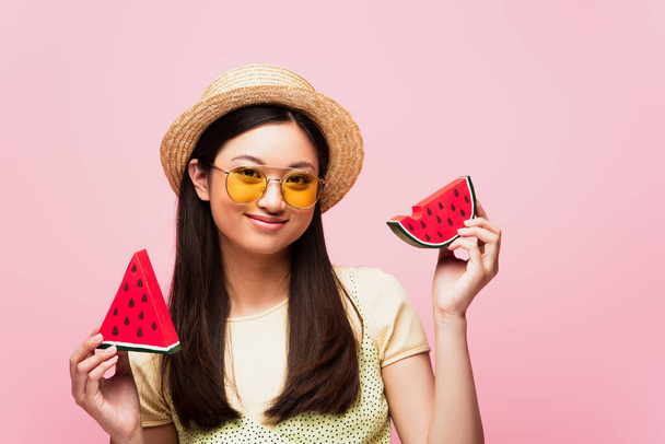 happy asian woman in sunglasses and straw hat holding sliced paper watermelon isolated on pink  - Fotoğraf, Görsel