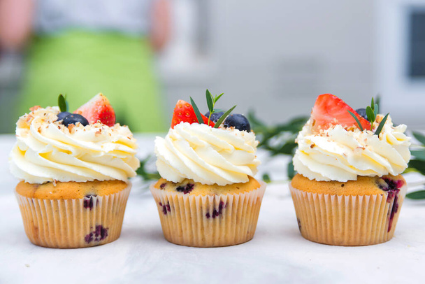 Tasty cupcakes decorated with cream cheese, blueberry and strawberry. Fruit cupcakes on modern concrete background. Sweet baked pastry. Holidays cupcakes with fruit. Sweet cupcakes for party. - Photo, Image