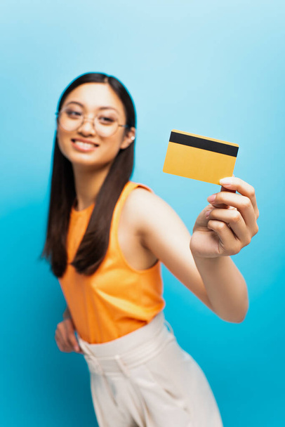 青の上にクレジットカードを保持しているメガネで幸せなアジアの女の子の選択的な焦点  - 写真・画像