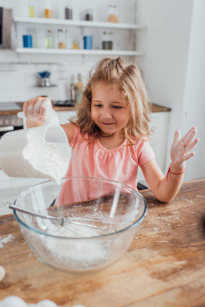 petite fille verser de la farine dans un bol en verre pendant la cuisson dans la cuisine - Photo, image