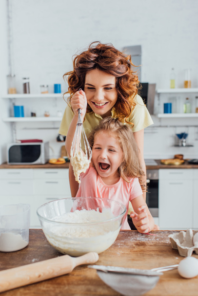 foyer sélectif de fille excitée tenant fouet avec pâte près de la mère - Photo, image