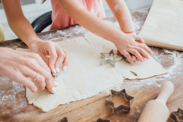 partial view of woman and child cutting out cookies from rolled dough near star-shaped molds - Photo, Image