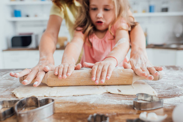 cropped view of daughter with nom rolling out dough near cookie cutters, selective focus - Foto, Imagem