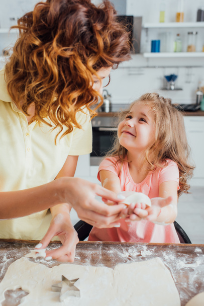 selective focus of mother holding raw cookie near daughter, rolled dough and star-shaped mold - Photo, Image