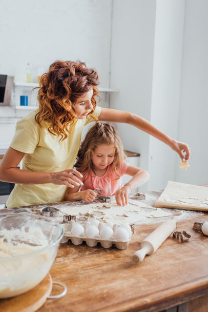 επιλεκτική εστίαση της μητέρας βάζοντας μπισκότο σε χαρτί ψησίματος κοντά στην κόρη  - Φωτογραφία, εικόνα