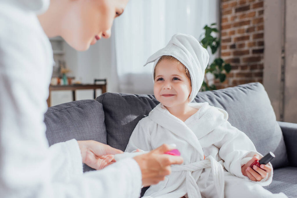 selective focus of woman making manicure to child in white bathrobe and towel on head - Photo, Image