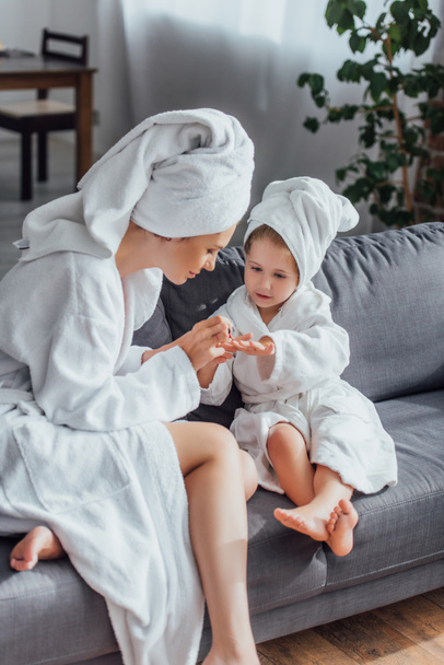 young woman making manicure to daughter while sitting in white bathrobes and towels on heads together - Valokuva, kuva