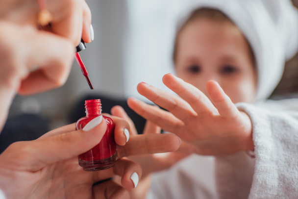 vista recortada de la mujer que aplica esmalte rojo en las uñas de la hija, enfoque selectivo - Foto, imagen