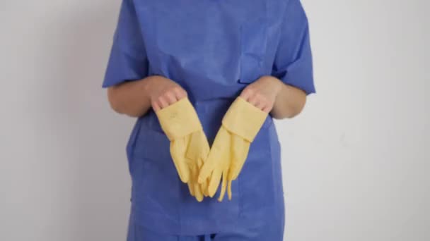 Показаны желтые латексные перчатки в руках в синем медицинском костюме - Кадры, видео
