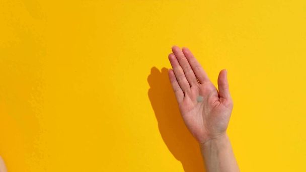 Una foto de la mano de una mujer con gel sobre un fondo amarillo - Foto, imagen