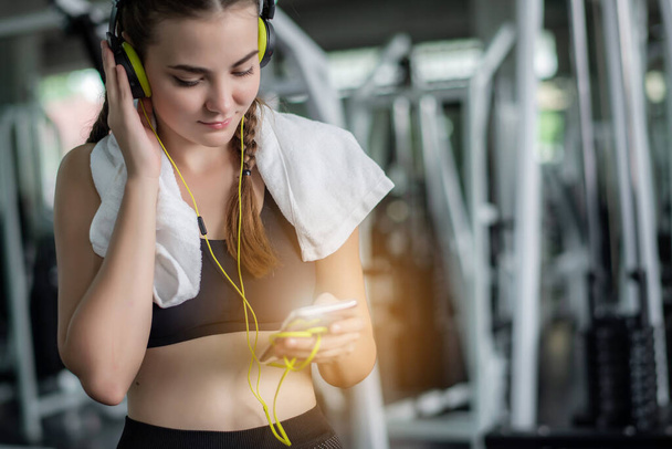 Young attractive woman listening to music by earphones connect to smart phone or cellphone. Relaxation after hard workout in gym  - Foto, afbeelding