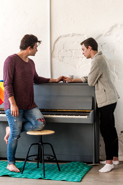 Δύο τύποι μιλάνε χέρι χέρι, στέκονται σε ένα δωμάτιο δίπλα σε ένα πιάνο. - Φωτογραφία, εικόνα