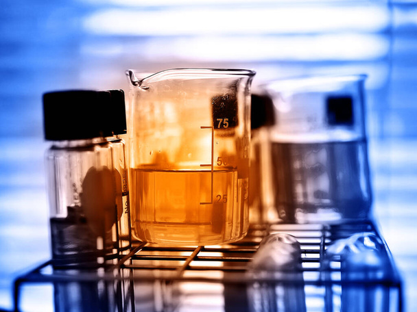 Γυάλινα αντικείμενα εργαστηρίου που περιέχουν χημικό υγρό με εργαστηριακό υπόβαθρο - Φωτογραφία, εικόνα