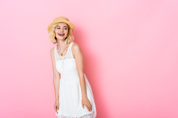 excited woman in straw hat laughing and looking away on pink  - Foto, Imagem