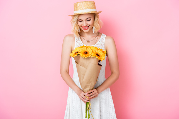Hasır şapkalı genç kadın pembe çiçeklere bakıyor.  - Fotoğraf, Görsel